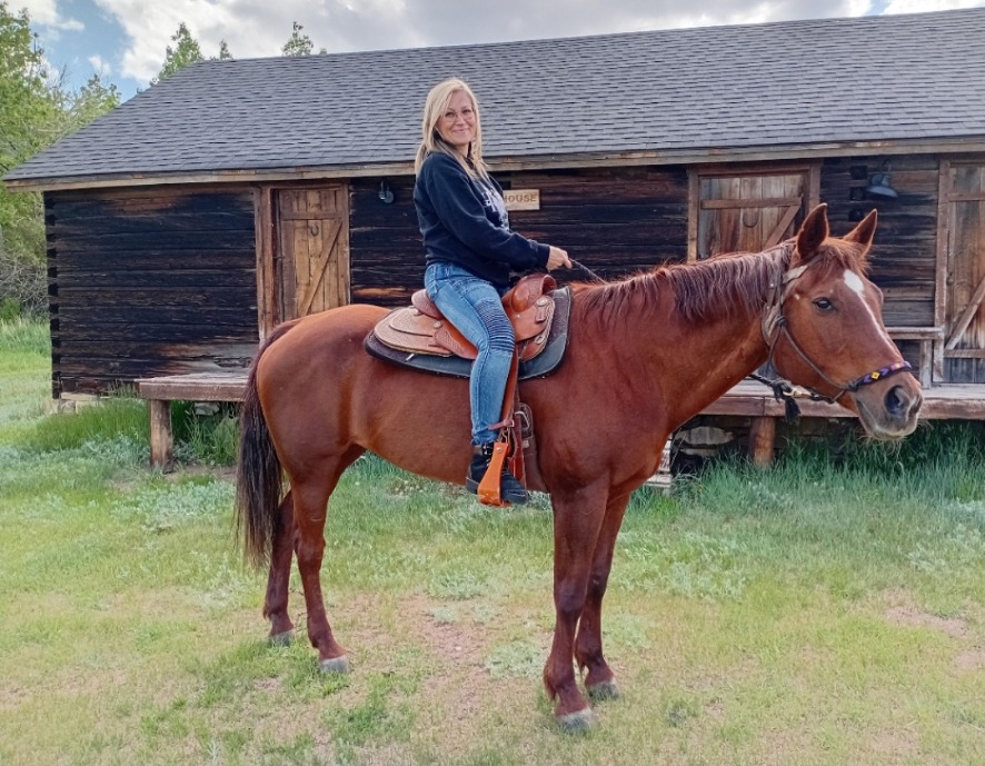 Jennifer on horseback in front of a rustic log barn